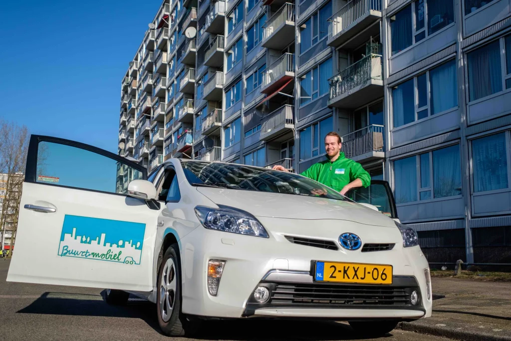 Chauffeur van gemeenschapsvervoerservice Buurt Mobiel staat bij auto voor een flat in Overvecht, in Utrecht