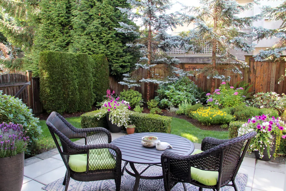 Tuin met een mooi terras, waarop tuinstoelen en een tuintafel staan met in de achtergrond allerlei planten