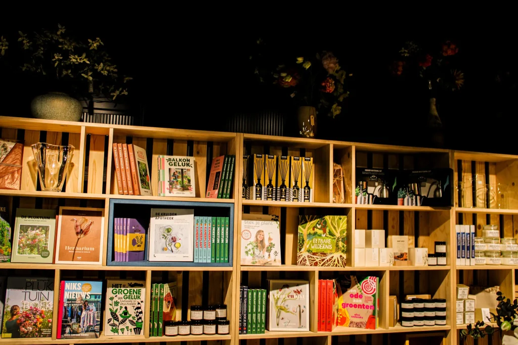 Afbeelding van een houten boekenkast in een winkel met diverse tuinboeken, verzorgingsproducten voor planten en enkele decoratieve items in de winkel van Oogst in Utrecht. Bloemen worden op de bovenste plank getoond.