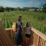 Vanaf de uitkijktoren in het Maisdoolhof kijken een moeder en dochter uit over het buitenterrein van Steck, met in beeld onder andere het maisdoolhof en tuincafé Noordertuin